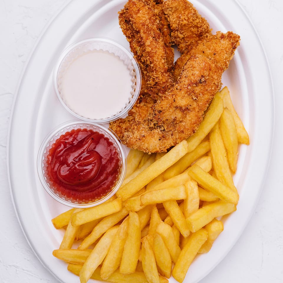Golden fried chicken tenders and crispy french fries with ketchup and a white dipping sauce.
