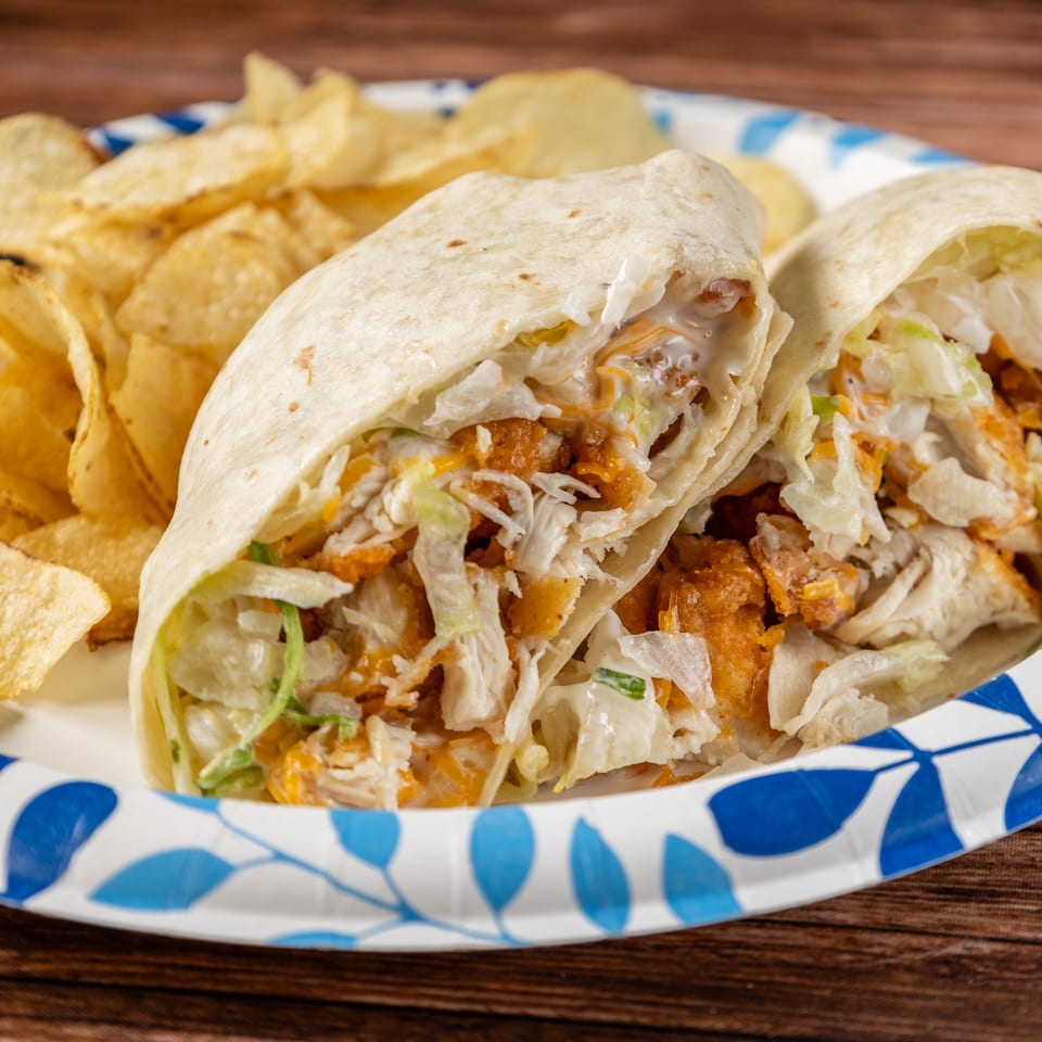 Two fried chicken wraps with shredded lettuce, cheese, and sauce, served with potato chips.