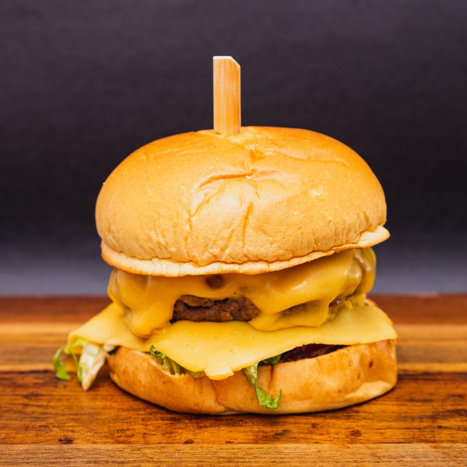 A Hitching Post double cheeseburger with melted cheese and lettuce on a wooden board.