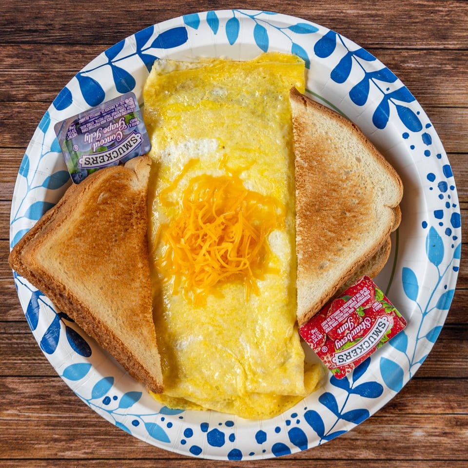 A breakfast plate with a cheese omelet, two slices of toast, grape jelly, and strawberry jam.